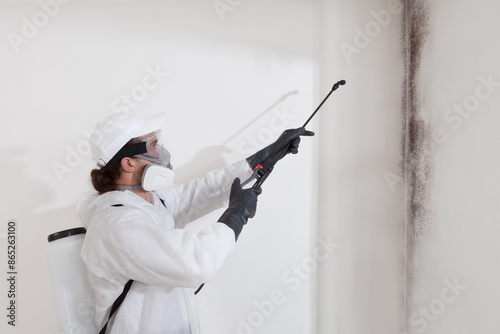 Mold remediation service: A professional worker spraying products to remove mold before house painting, clad in a protective suit and respirator mask, with a backpack sprayer at a home renovation site photo