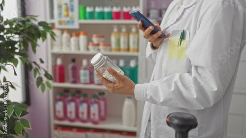 A woman pharmacist in a white coat uses her phone to photograph a medicine bottle in a pharmacy filled with various health and beauty products. photo