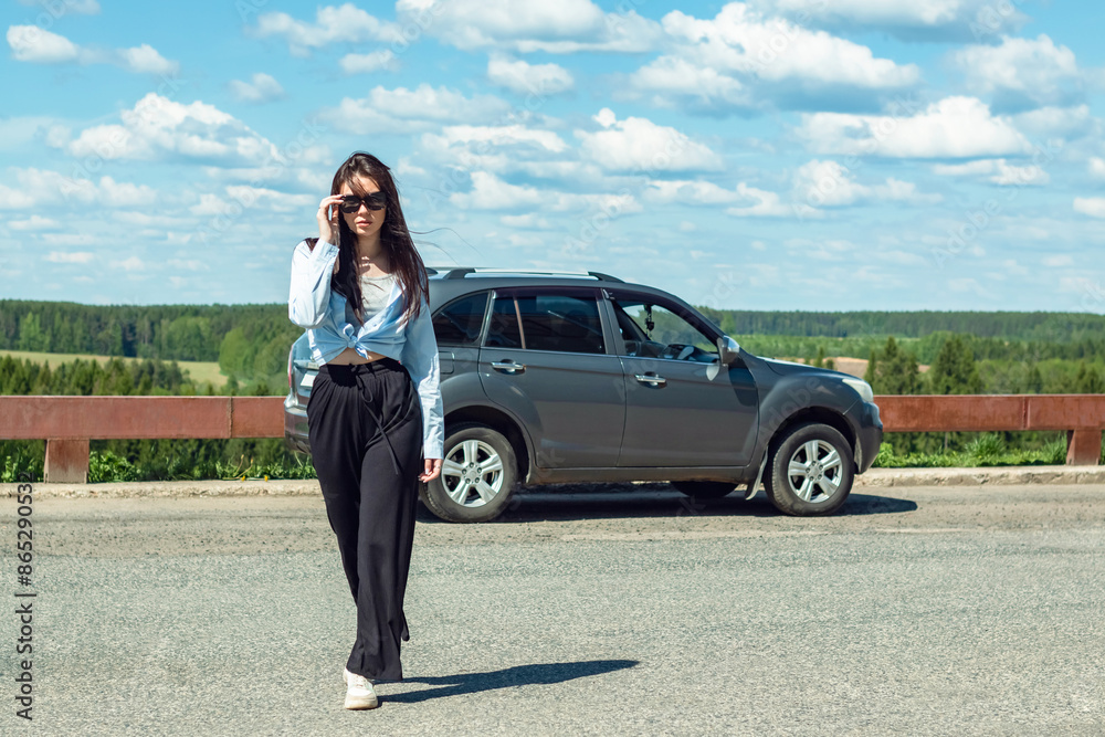 A girl in sunglasses stands by a car.