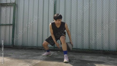 Young Asian Male Basketball Player Practicing Ball Handling Skill, Dribbling Ball Between The Legs On Outdoor Court