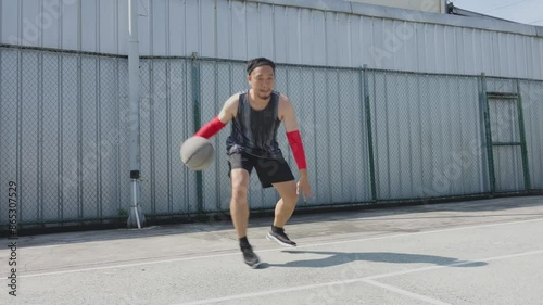 Rear View Of Asian Man Basketball Player Practicing Ball Handling Skill, Dribbling Ball Between Legs On Outdoor Court 