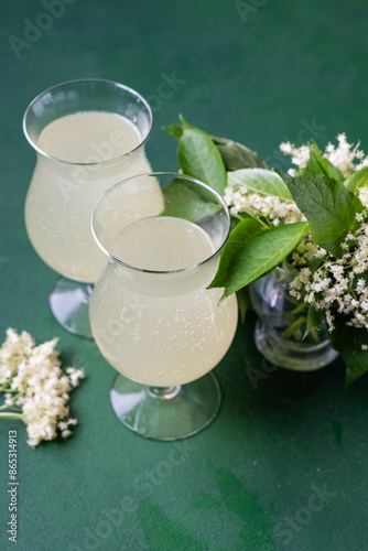 Carbonated elderflower drink. Flower summer kvass in glasses. Sparkling homemade hugo water. Buza drinks in two glass on green background