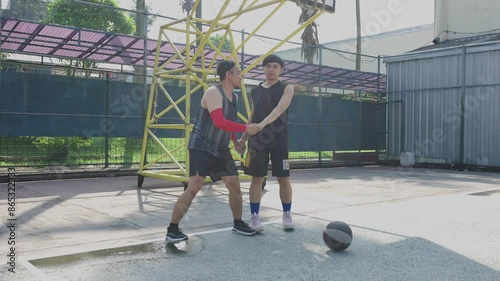 Two Young Asian Men Warming Up Before Playing Basketball On Outdoor Court 