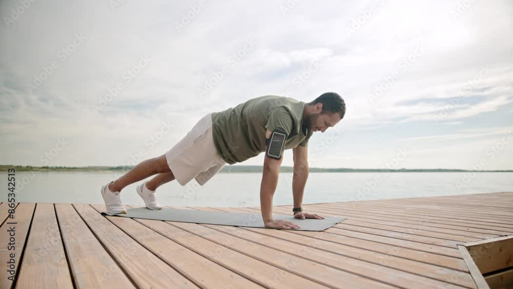 Camera view from side of African American male standing in plank position with focus. Working out on fresh air on pierce. Huge lake around male. Trying to beat his personal record. Camera view from side of African American male standing in plank position with focus. Working out on fresh air on pierce. Huge lake around male. Trying to beat his personal record.