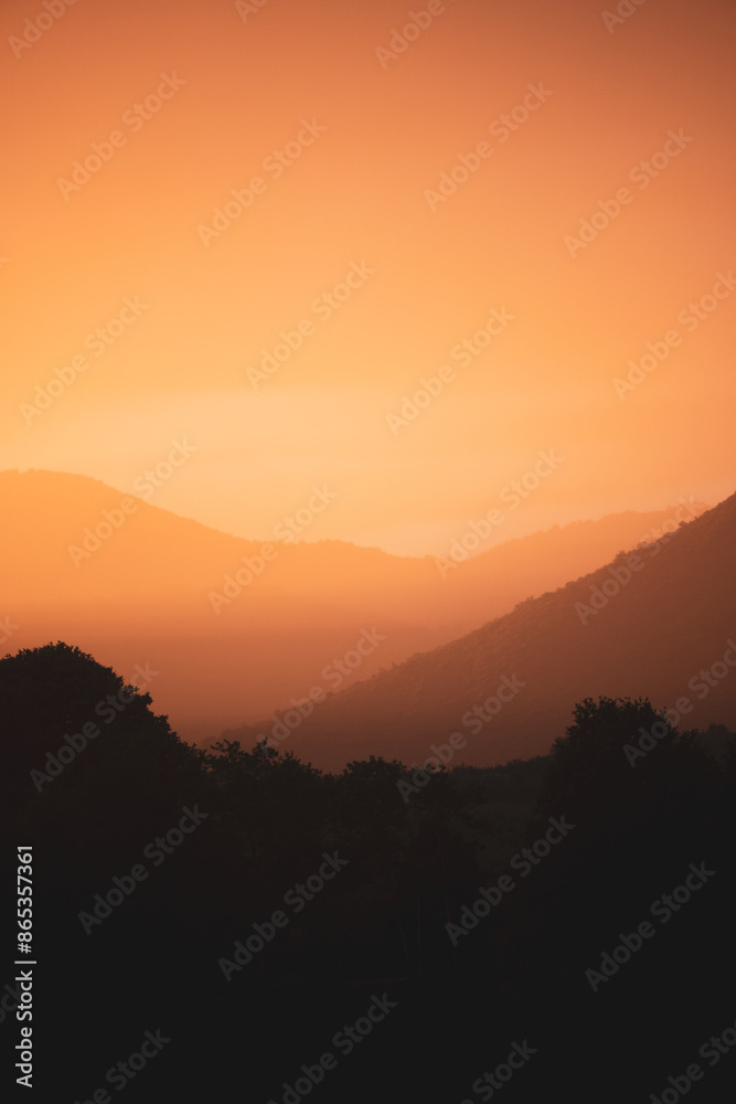 Stunning view of a dramatic sunset with beautiful shades of orange, silhouette of mountains in foreground and in the distance.