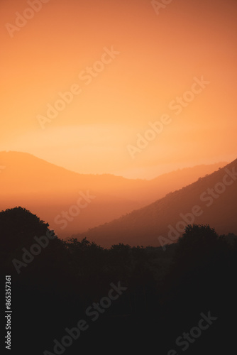 Obraz na płótnie Stunning view of a dramatic sunset with beautiful shades of orange, silhouette of mountains in foreground and in the distance. w salonie