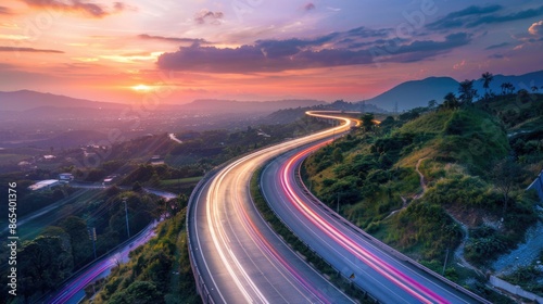 Long exposure shot of car light trails on highway at colorful sunset in mountainous area. © Grigor