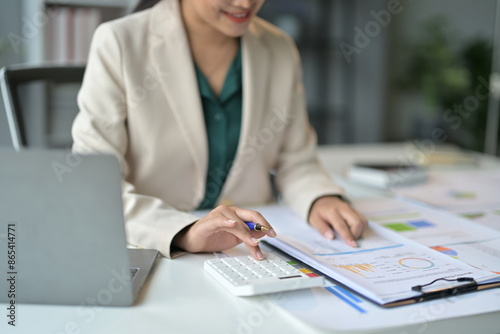 Businesswoman is analyzing a financial chart at her desk in the office. She is using a calculator to help her with her calculations