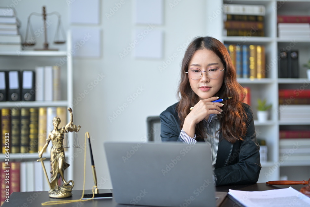 Lawyer working in her office with a laptop, law books, and a statue of lady justice, symbolizing her dedication to legal work Lawyer working in her office with a laptop, law books, and a statue of lady justice, symbolizing her dedication to legal work