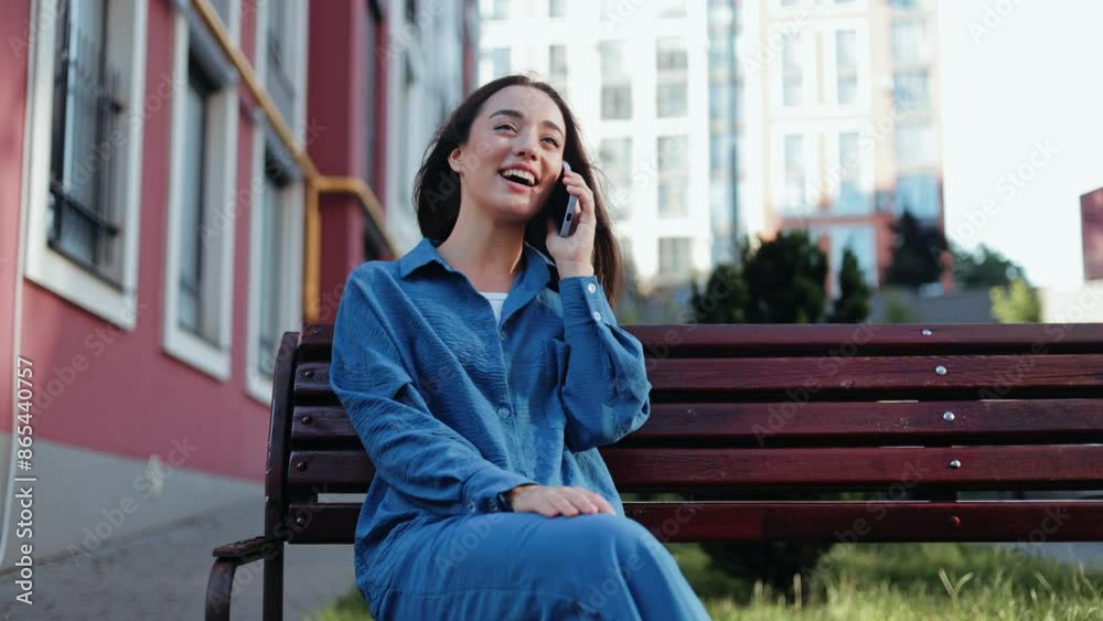 Smiling woman enjoys a phone call while sitting on a bench.