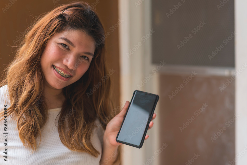 Asian woman in her 30s standing outside her apartment flat, showing off a cellphone app. Blank phone screen for editing. Asian woman in her 30s standing outside her apartment flat, showing off a cellphone app. Blank phone screen for editing.
