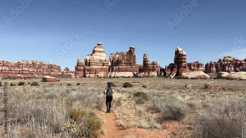Slow motion tracking shot of a female hiker walking towards the needles sandstone formations in Canyonlands National Park, Utah. The beautiful desert landscape stretches out before her - USA