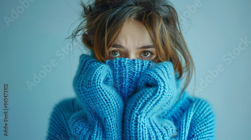 Woman wearing blue turtleneck knitted sweater sadly look at camera while covering sad face. Feelings of depression, sadness, loneliness, social phobia photo