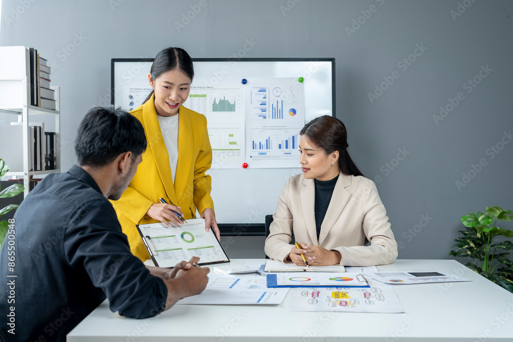 Three people are sitting at a table with a white board behind them Three people are sitting at a table with a white board behind them