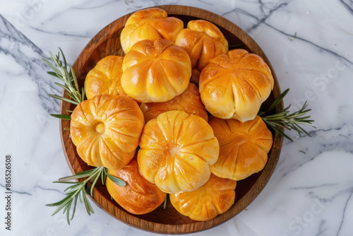 top view, pumpkin-shaped dinner rolls on wooden platter with rosemary accents , marble surface