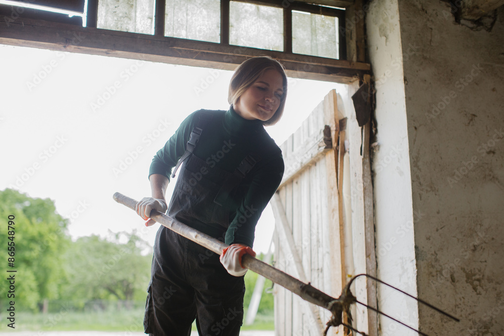 A woman worker with a pitchfork in her hands works in a cowshed on a farm.