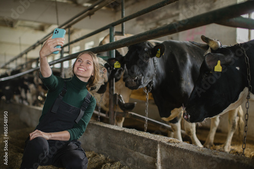 A young female farmer takes a selfie with cows on a mobile phone.