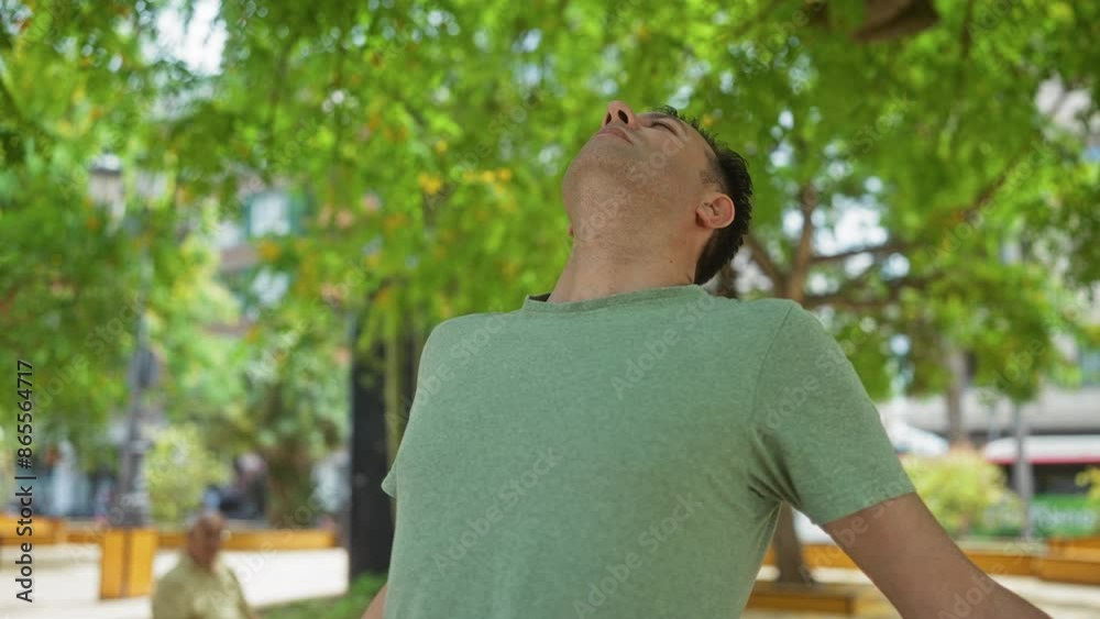 Man breathing deeply in a green shirt standing outdoors in a city park with lush green trees Man breathing deeply in a green shirt standing outdoors in a city park with lush green trees