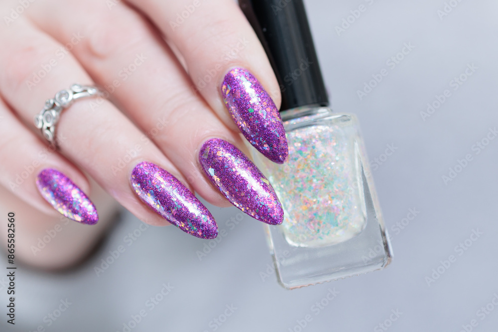 Woman hand with long nails and a bottle of plum purple nail polish Woman hand with long nails and a bottle of plum purple nail polish