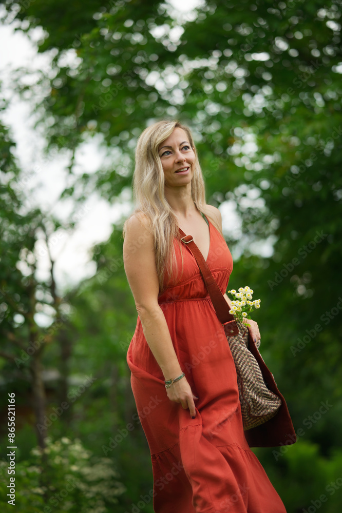 Natural blond Woman walks though a green garden, wearing a red long dress, smiling Natural blond Woman walks though a green garden, wearing a red long dress, smiling