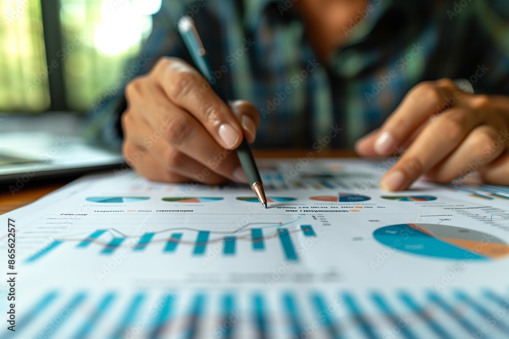 A person is writing on a piece of paper with a pencil. The paper has a lot of graphs and numbers on it. The person seems to be focused on the graphs and numbers A person is writing on a piece of paper with a pencil. The paper has a lot of graphs and numbers on it. The person seems to be focused on the graphs and numbers