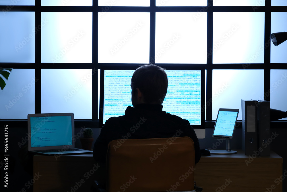 Hacker using computer at table in dark room, back view Hacker using computer at table in dark room, back view