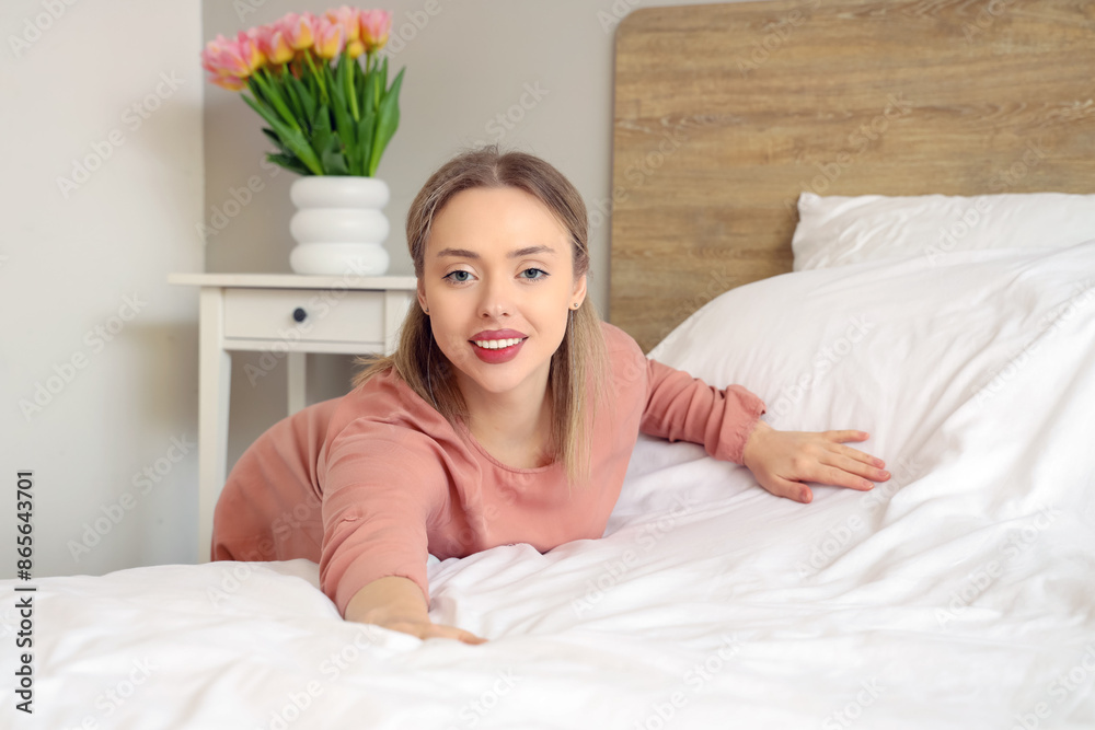 Pretty young woman making bed in light bedroom Pretty young woman making bed in light bedroom