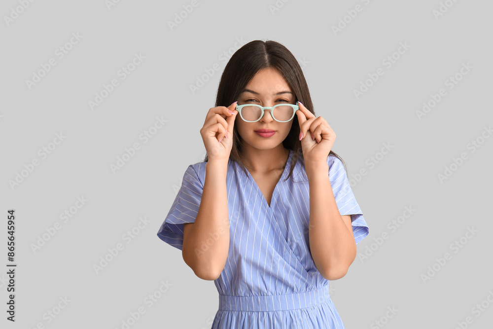 Beautiful young Asian woman with new eyeglasses on grey background Beautiful young Asian woman with new eyeglasses on grey background