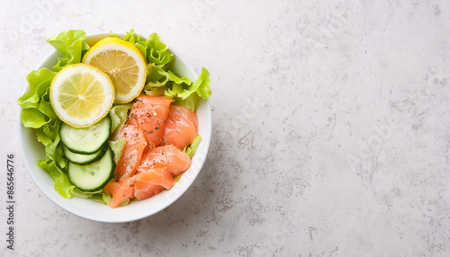 Bowl of salted salmon with fresh lettuce, cucumbers and lemon slices. Ketogenic-friendly lunch.