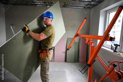 Foto Construction worker carrying a large plasterboard with the help of a drywall lif