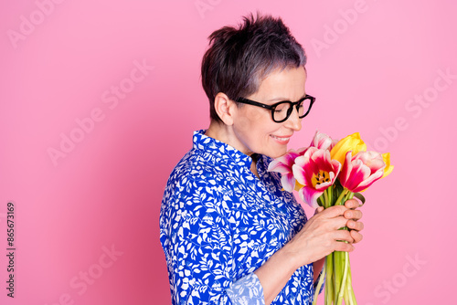Photo of good mood senior person with white gray hairstyle dressed print blouse smell colorful tulips isolated on pink color background photo