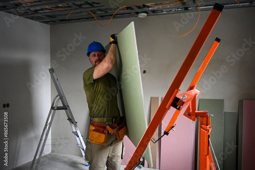 Obraz na płótnie Construction worker carrying a large plasterboard with the help of a drywall lif