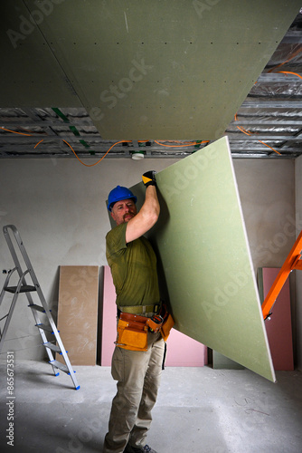 Construction worker carrying a large plasterboard with the help of a drywall lift, on a construction site photo