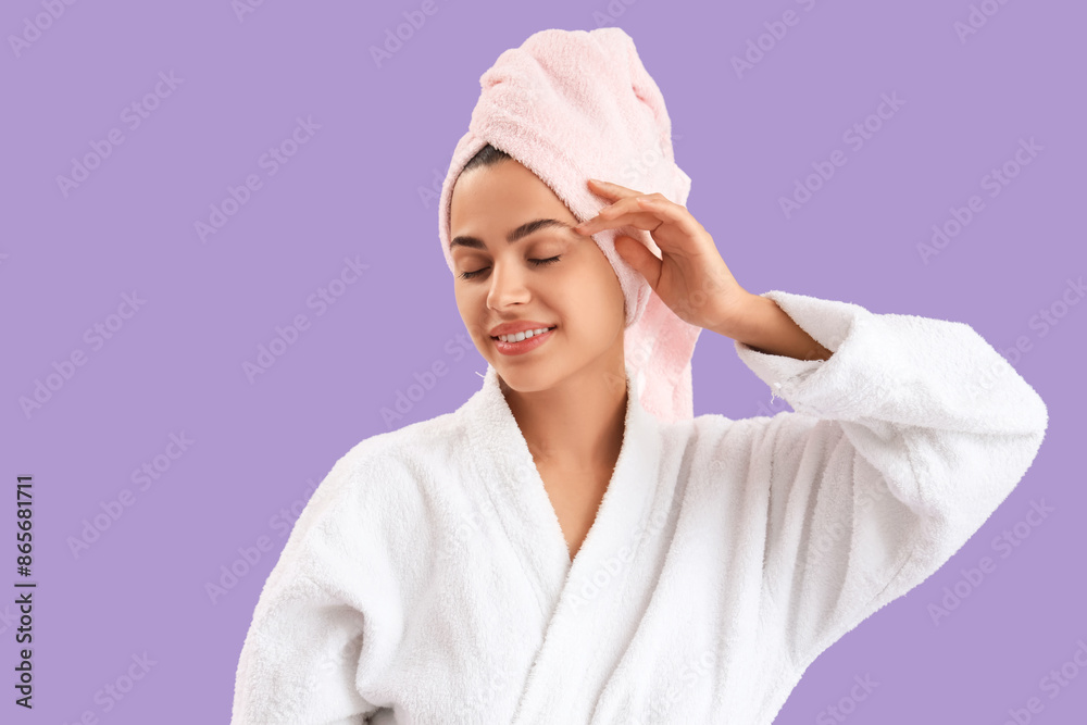 Beautiful young happy woman in bathrobe with towel on purple background
