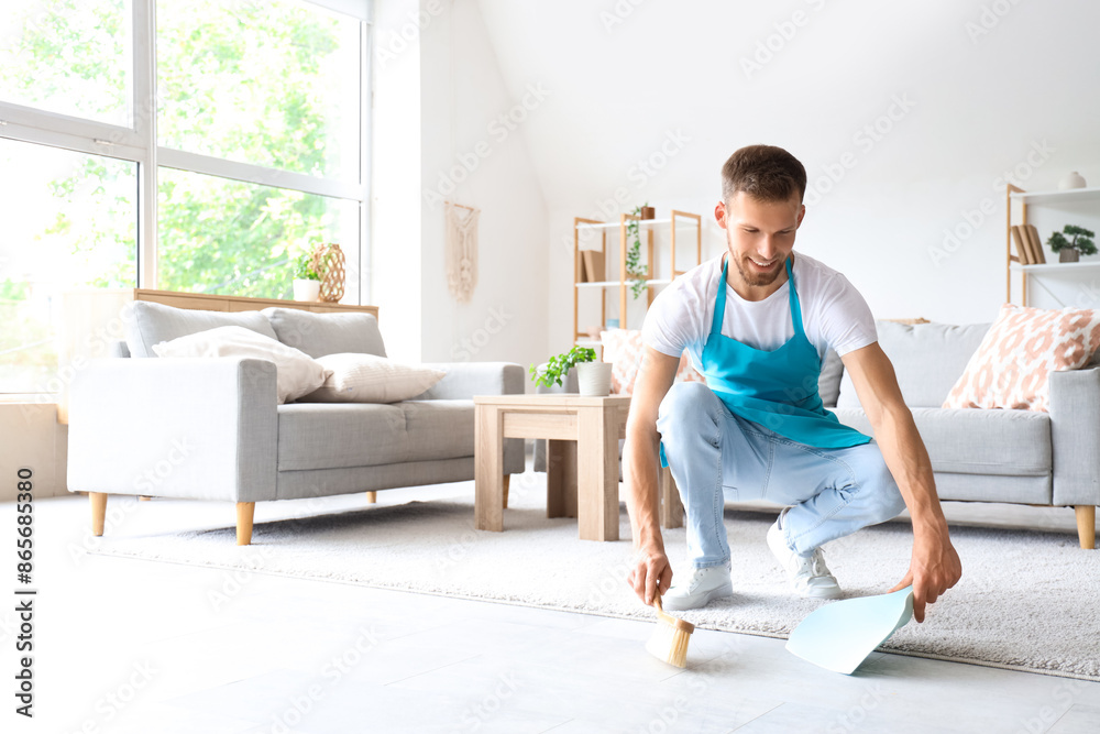 Male janitor with dust pan and brush cleaning floor in light room Male janitor with dust pan and brush cleaning floor in light room