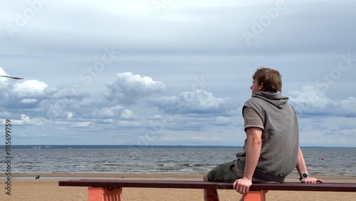 Young man sitting on a bench on beach and enjoying sea view