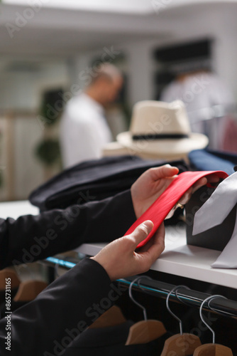 Woman seller hands putting red tie on accessory shelf while organizing merchandise in clothing store closeup. Mall employee arms examining garment while working in apparel outlet