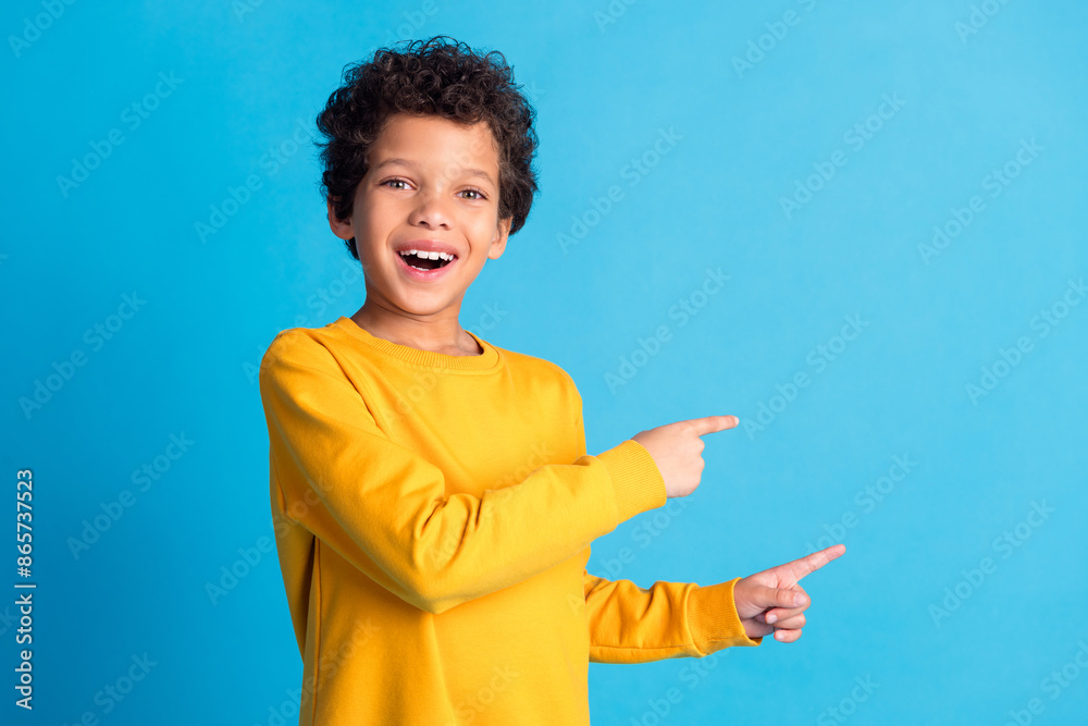 Portrait of cute small schoolkid point fingers empty space wear pullover isolated on blue color background Portrait of cute small schoolkid point fingers empty space wear pullover isolated on blue color background
