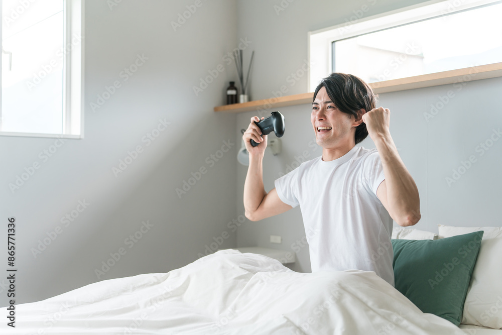家のベッドルーム・寝室でゲームをする男性ゲーマー（笑顔）
