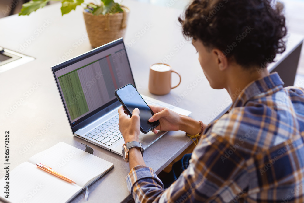 Using smartphone while working on laptop, teenage boy multitasking at home office Using smartphone while working on laptop, teenage boy multitasking at home office