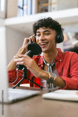 Recording podcast, smiling young man using microphone and laptop at home studio