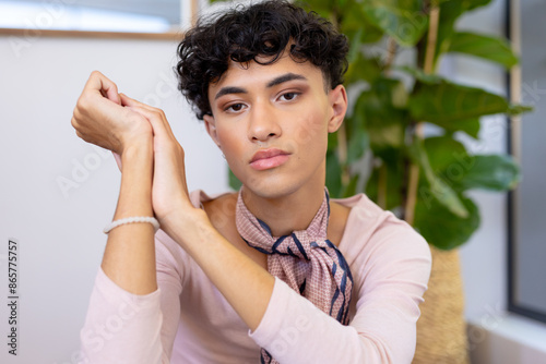 Posing indoors, transgender transgender woman sitting with thoughtful expression, wearing scarf