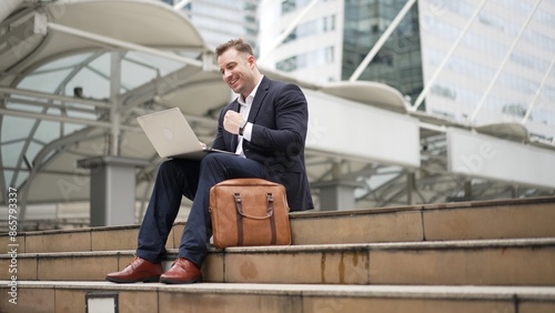 Close up of business man talking phone and celebrate successful project while sitting at stairs surrounded by urban city view. Smart caucasian manager happy while hear about increasing sales. Urbane.