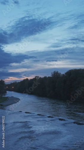 Munich at dramatic dusk sunset. View of Isar river, trees and St Maximilian church from Reichenbach Bridge in Autumn. Munchen, Bavaria, Germany. Camera horizontal pan photo