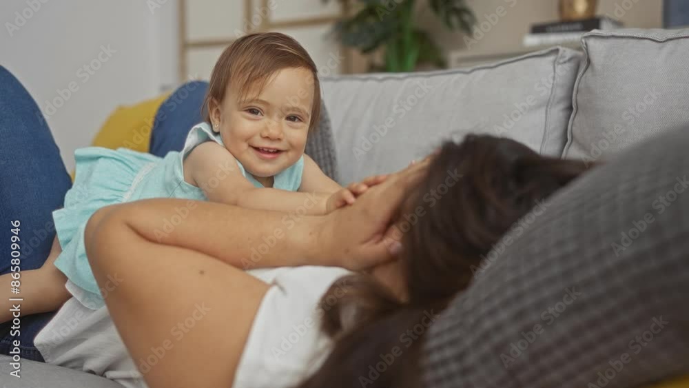 Woman relaxing indoors with her toddler daughter, enjoying playful moments together on the living room couch. Woman relaxing indoors with her toddler daughter, enjoying playful moments together on the living room couch.