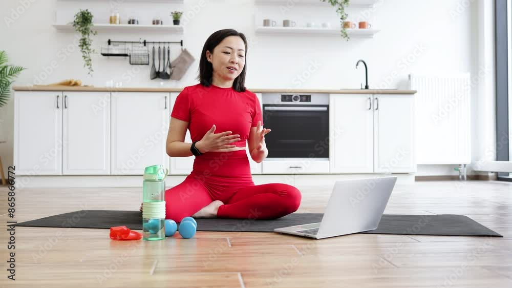 Woman in red sportswear practicing yoga in modern kitchen setting while following virtual instructions from laptop. Health, wellness, and mindfulness focus with water bottle and exercise equipment. Woman in red sportswear practicing yoga in modern kitchen setting while following virtual instructions from laptop. Health, wellness, and mindfulness focus with water bottle and exercise equipment.