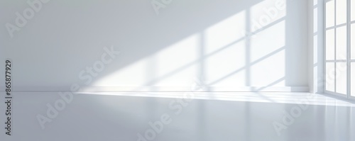 An empty white room with large windows casting natural light and shadows on the floor, creating a minimalist and serene atmosphere.