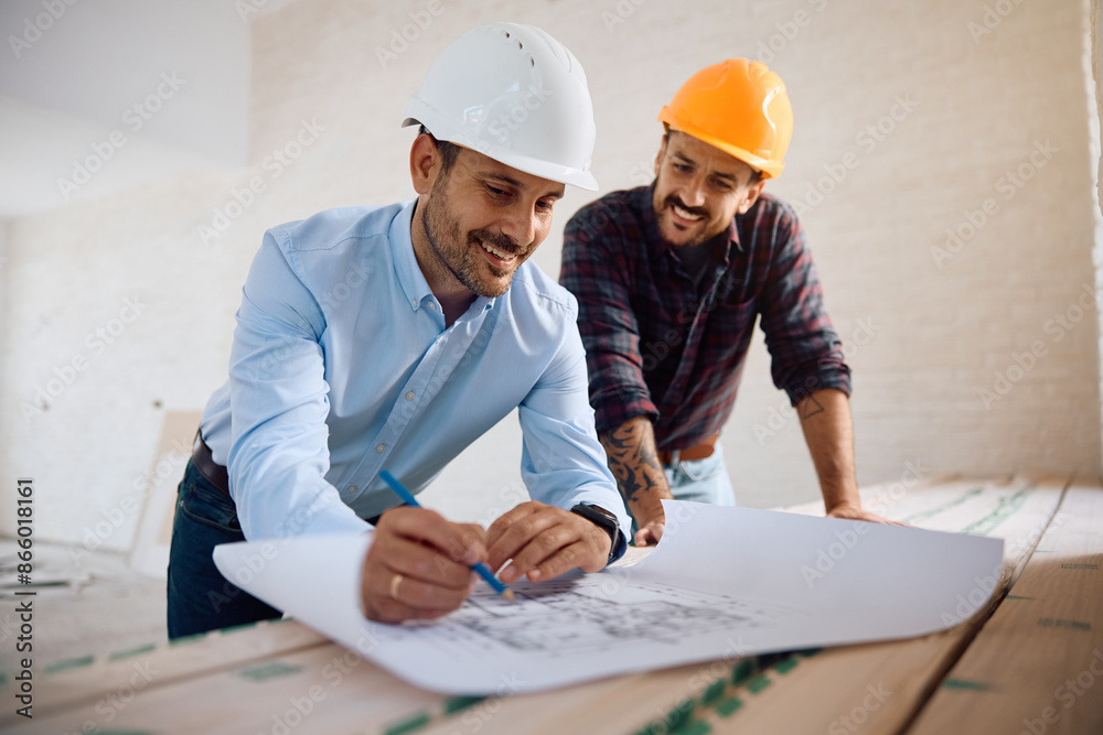 Happy architect and construction site worker cooperating while analyzing blueprints.