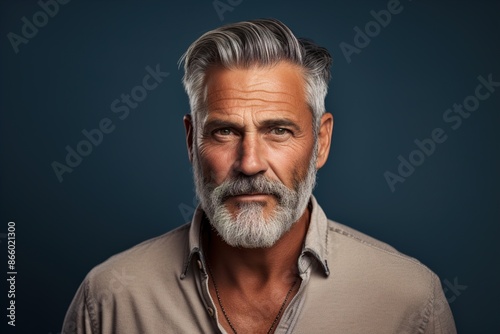 A man with a beard and gray hair is wearing a tan shirt