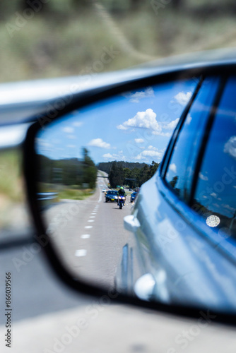 Blurred image of car side mirror showing motorbike rider on highway